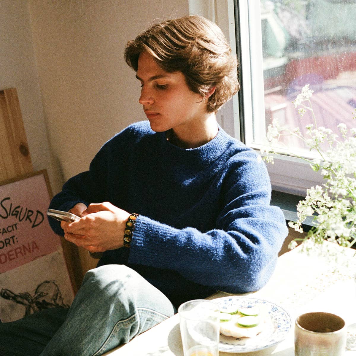 En student sitter med mobilen vid frukostbordet hemma